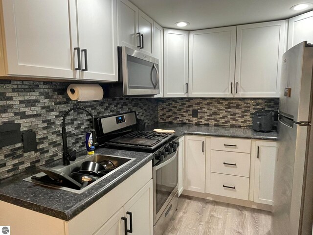 kitchen featuring decorative backsplash, white cabinets, stainless steel appliances, and light wood-type flooring