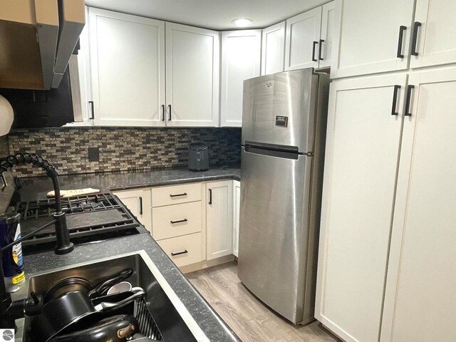 kitchen with stainless steel fridge, white cabinetry, light hardwood / wood-style flooring, and backsplash