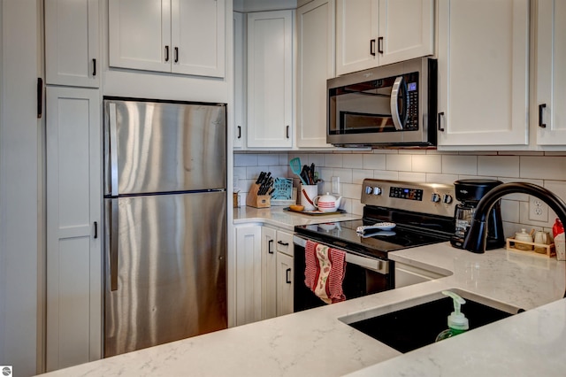 kitchen featuring white cabinetry, light stone countertops, appliances with stainless steel finishes, and backsplash