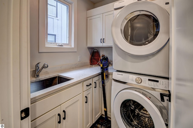 clothes washing area featuring sink, stacked washer and clothes dryer, and cabinets