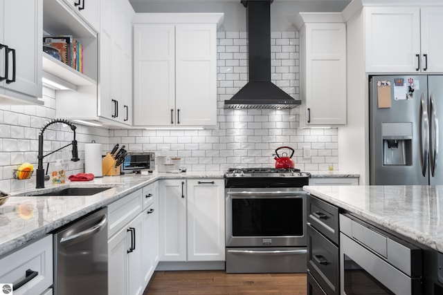 kitchen with light stone countertops, wall chimney exhaust hood, stainless steel appliances, sink, and white cabinetry