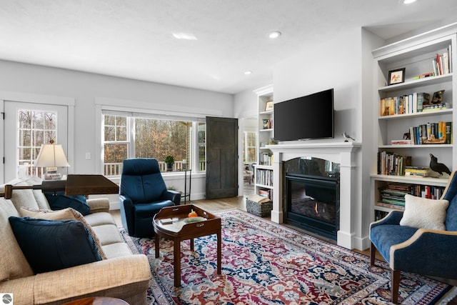 living room featuring built in shelves, a premium fireplace, and wood-type flooring