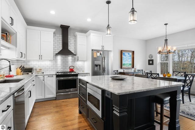 kitchen featuring white cabinets, wall chimney exhaust hood, a center island, and appliances with stainless steel finishes