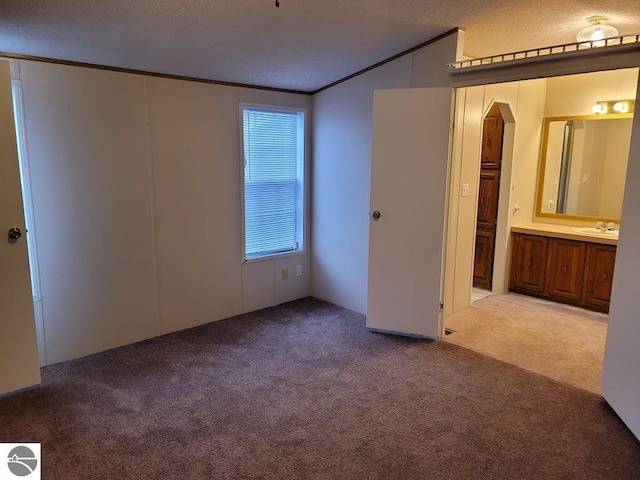 unfurnished bedroom featuring a textured ceiling, light carpet, crown molding, and connected bathroom