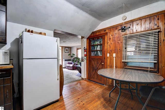 dining space with wooden walls, hardwood / wood-style floors, vaulted ceiling, and a textured ceiling