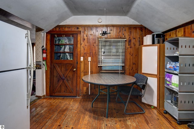 dining space with dark hardwood / wood-style flooring, wooden walls, and vaulted ceiling