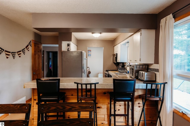 kitchen with stainless steel appliances, white cabinetry, kitchen peninsula, a kitchen breakfast bar, and light wood-type flooring