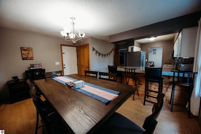 dining area with light hardwood / wood-style floors, a notable chandelier, and a textured ceiling