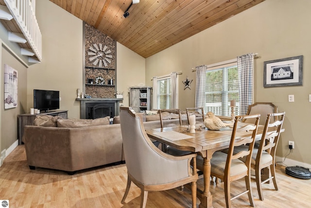 dining area with a large fireplace, high vaulted ceiling, wood ceiling, and light wood-type flooring