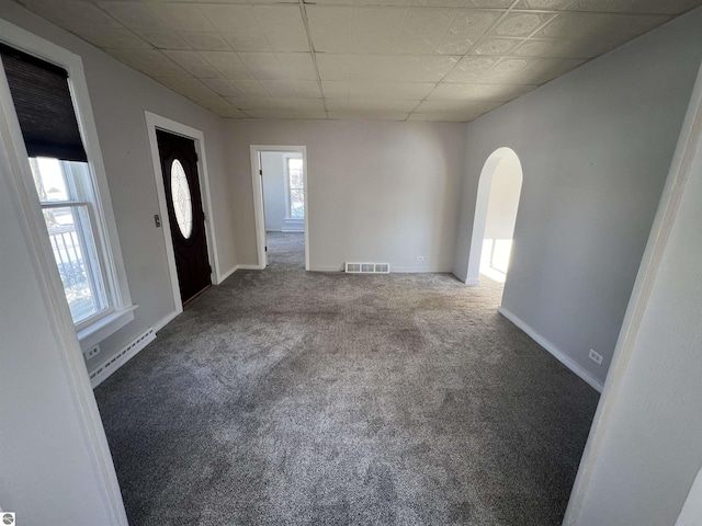 carpeted empty room with a wealth of natural light, a drop ceiling, and a baseboard heating unit