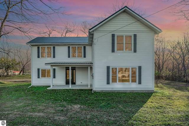 back house at dusk with a patio area and a yard