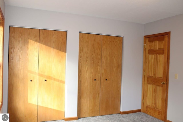 unfurnished bedroom featuring multiple closets and light colored carpet