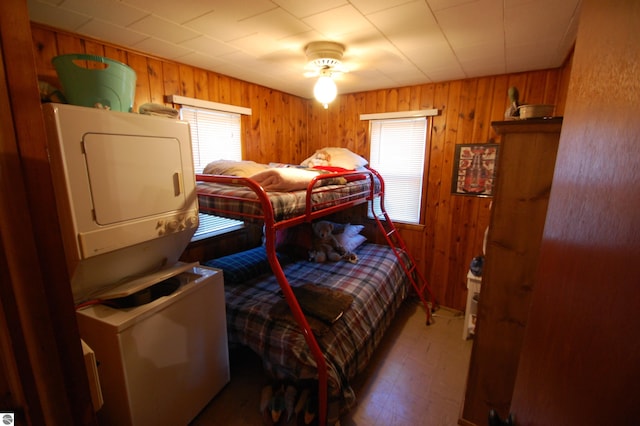 bedroom featuring stacked washer and dryer, wooden walls, and ceiling fan