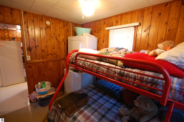 bedroom featuring wood walls and white refrigerator