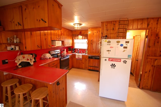 kitchen featuring kitchen peninsula, wooden walls, white appliances, and a breakfast bar