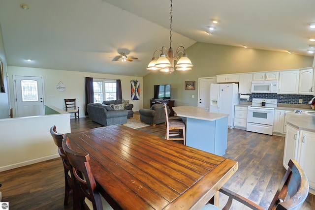 dining space featuring dark wood-type flooring, ceiling fan with notable chandelier, sink, and vaulted ceiling