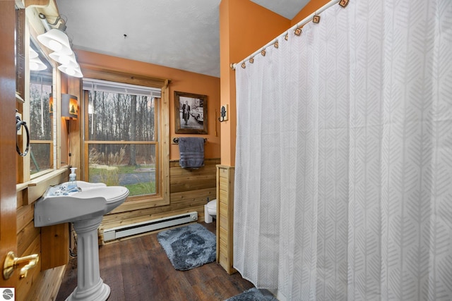 bathroom with a textured ceiling, wood walls, hardwood / wood-style flooring, toilet, and baseboard heating