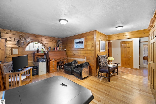 living room with light hardwood / wood-style floors, wooden walls, and a textured ceiling