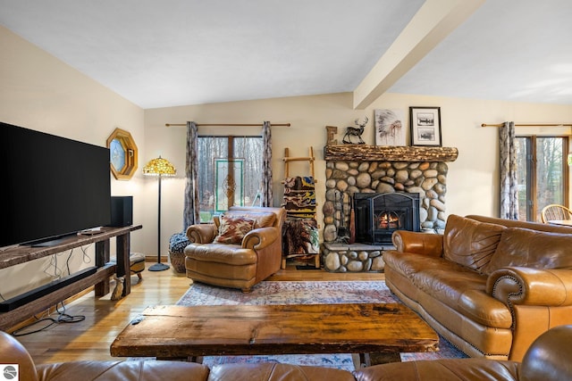 living room with lofted ceiling with beams, a wealth of natural light, light hardwood / wood-style floors, and a stone fireplace