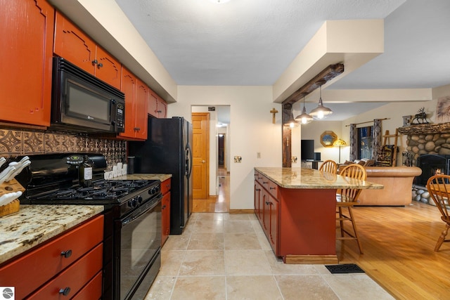 kitchen with hanging light fixtures, black appliances, a breakfast bar, a fireplace, and light hardwood / wood-style flooring