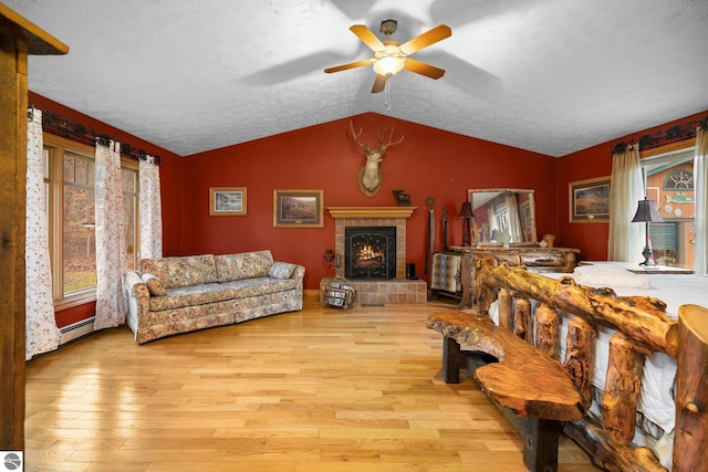 living room with ceiling fan, a textured ceiling, light hardwood / wood-style flooring, a tile fireplace, and vaulted ceiling