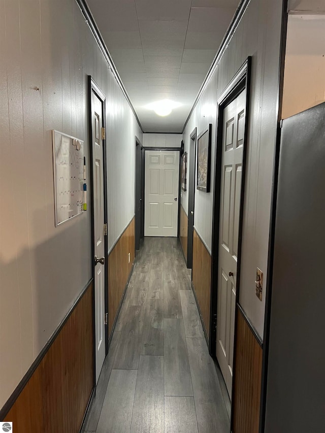 hallway with dark hardwood / wood-style floors, wooden walls, and ornamental molding