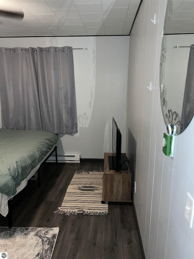 bedroom featuring baseboard heating, a paneled ceiling, dark wood-type flooring, and wooden walls