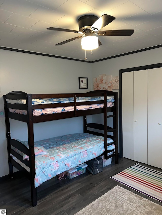 bedroom featuring dark wood-type flooring, ceiling fan, crown molding, and a closet