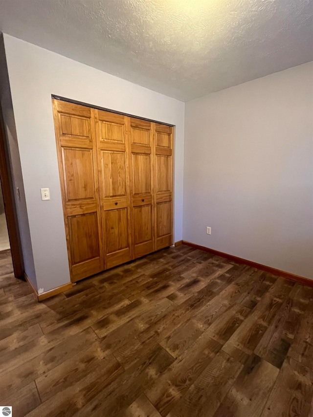 unfurnished bedroom with a textured ceiling, dark hardwood / wood-style flooring, and a closet