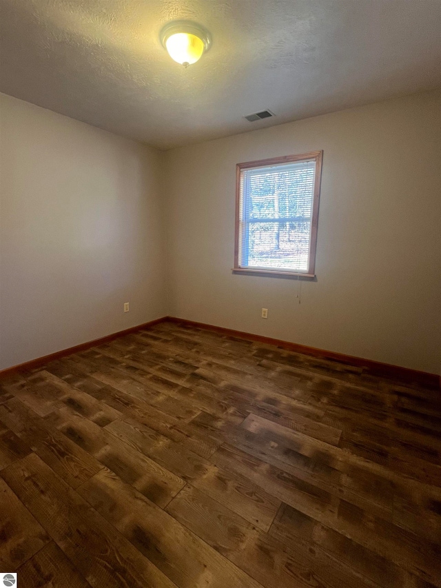 empty room with dark hardwood / wood-style flooring and a textured ceiling