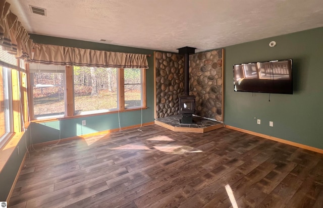 unfurnished living room featuring plenty of natural light, wood-type flooring, a wood stove, and a textured ceiling