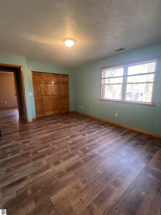 unfurnished bedroom featuring a textured ceiling, a closet, and dark hardwood / wood-style floors