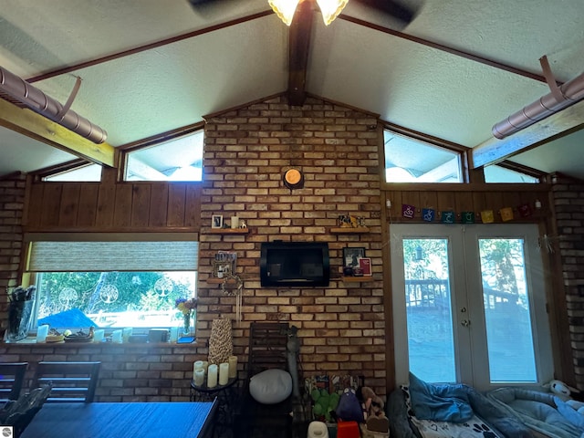 unfurnished living room featuring a textured ceiling, brick wall, vaulted ceiling with beams, and french doors