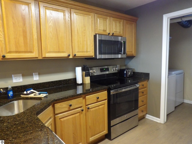 kitchen featuring stainless steel appliances, dark stone counters, sink, light hardwood / wood-style flooring, and washing machine and dryer