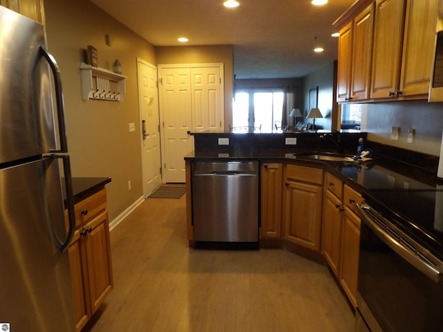 kitchen with sink, kitchen peninsula, appliances with stainless steel finishes, dark stone countertops, and light hardwood / wood-style flooring