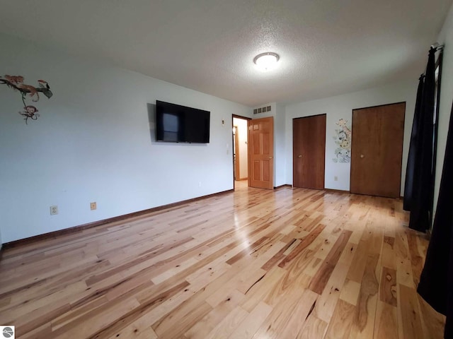 unfurnished bedroom with multiple closets, a textured ceiling, and light wood-type flooring