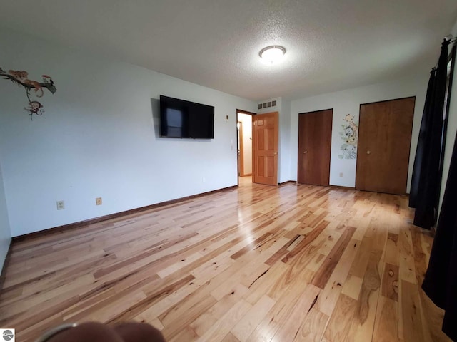 unfurnished bedroom with light hardwood / wood-style floors, a textured ceiling, and multiple closets