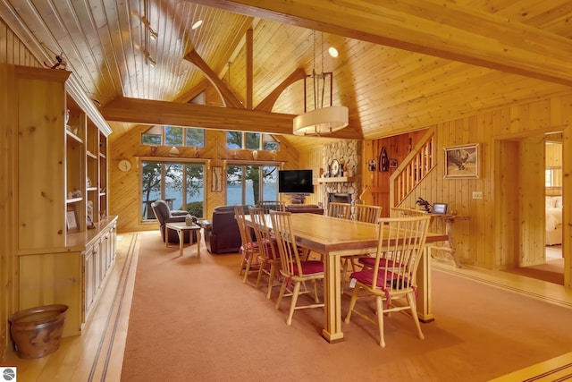 carpeted dining area featuring beam ceiling, high vaulted ceiling, a stone fireplace, and wood walls