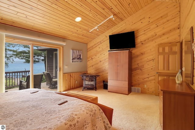 carpeted bedroom featuring access to exterior, track lighting, vaulted ceiling, a water view, and wood walls