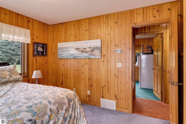 bedroom with carpet floors, stainless steel refrigerator, and wood walls