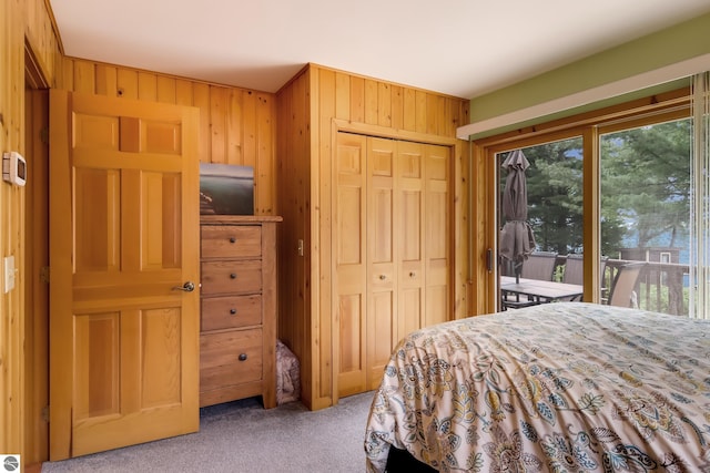 bedroom featuring light carpet, access to outside, a closet, and wood walls