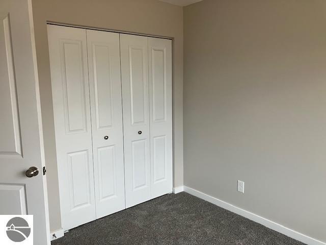 unfurnished bedroom with dark carpet and a closet