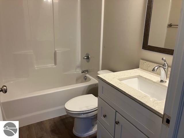 full bathroom featuring washtub / shower combination, vanity, hardwood / wood-style flooring, and toilet