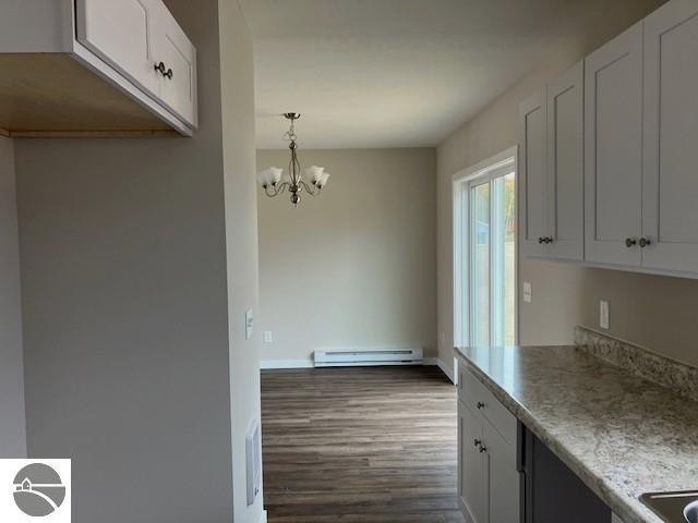 kitchen with white cabinetry, baseboard heating, hardwood / wood-style floors, hanging light fixtures, and a notable chandelier