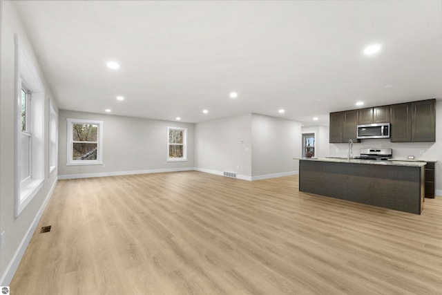 kitchen featuring dark brown cabinets, stainless steel appliances, an island with sink, and light hardwood / wood-style flooring