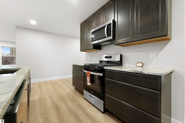 kitchen with appliances with stainless steel finishes, light stone counters, dark brown cabinets, sink, and light hardwood / wood-style flooring