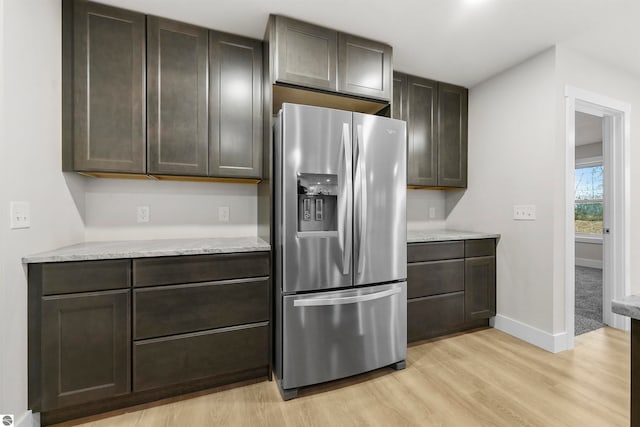 kitchen with light stone counters, dark brown cabinets, stainless steel refrigerator with ice dispenser, and light wood-type flooring