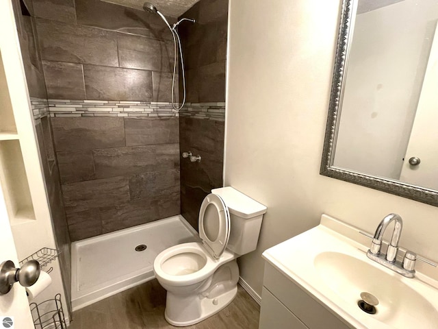 bathroom featuring a tile shower, hardwood / wood-style floors, vanity, and toilet