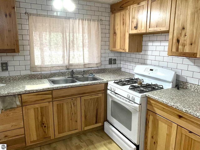 kitchen with backsplash, gas range gas stove, sink, and light hardwood / wood-style floors