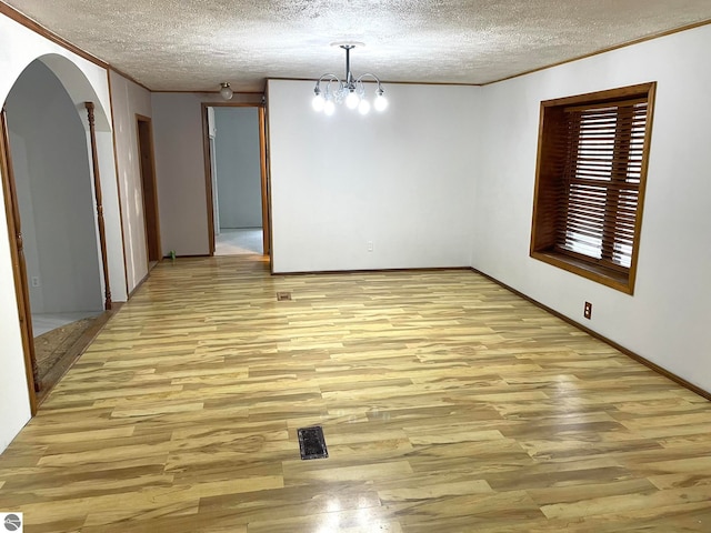 unfurnished dining area featuring light hardwood / wood-style flooring, a textured ceiling, ornamental molding, and an inviting chandelier